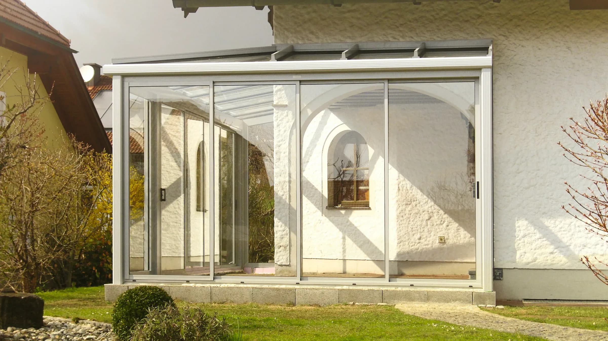 Terrassendach mit verglasten Seitenwänden an einem weißen Haus